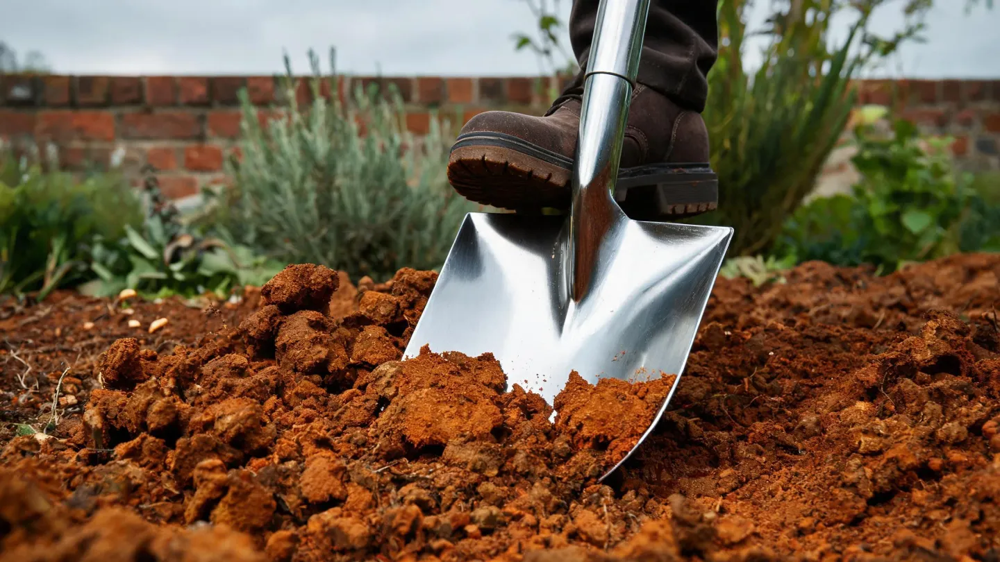 A stainless steel spade slicing into heavy clay soil